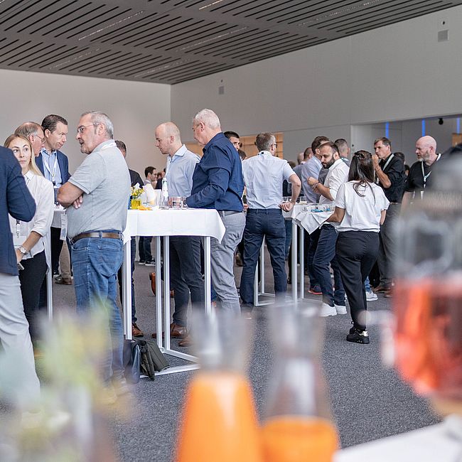 Business people in conversation at standing tables during a networking event in a modern event room