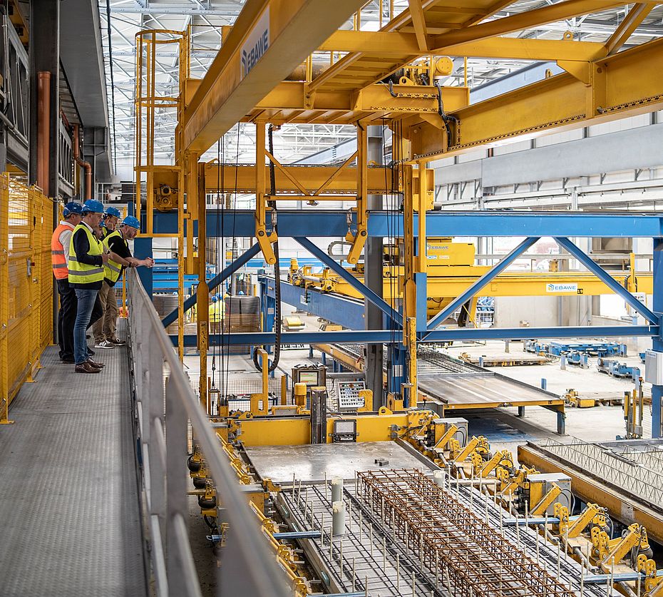 Employees with safety helmets observe an EBAWE production system for precast concrete production in a workshop hall